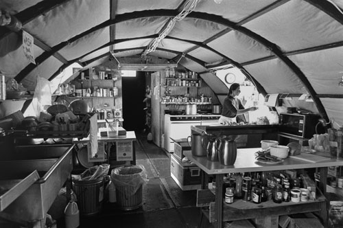 <p>Tanya Zastrow prepares lunch in the Siple Dome galley. Located 600 miles east of McMurdo, this "Jamesway" was assembled as part of a temporary camp hurriedly assembled to accommodate 50 people for the season.</p><p>"When they first flew us in it was 35 below F and cold; windy and cold. On a ’put-in’ the first thing you do is go for creature comforts. You get the tents up, shelter and food. Everything was buried, just the pallets sticking out. There’s a certain amount that just has to be done quickly because it is so damn cold. The galley is always the first building you put up. Jay Burnside, the construction foreman, is a driven, hardworking, ’balls to the wall’ sort of guy, so everybody he picks for a put-in tends to be that way."<br/>—Richard Flanders, Siple Dome camp manager</p>